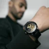 Hombre con Reloj negro con mecanismo en dorado.